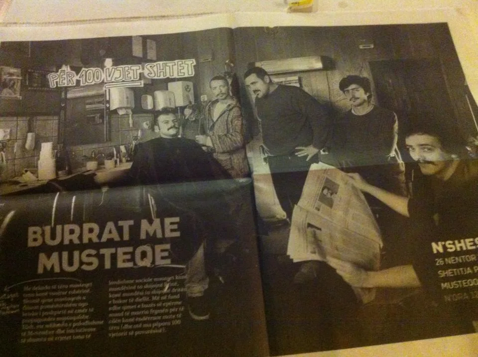 The "Burrat me Musteqe" spread as it ran in print, a double page in a newspaper photographed on a table.