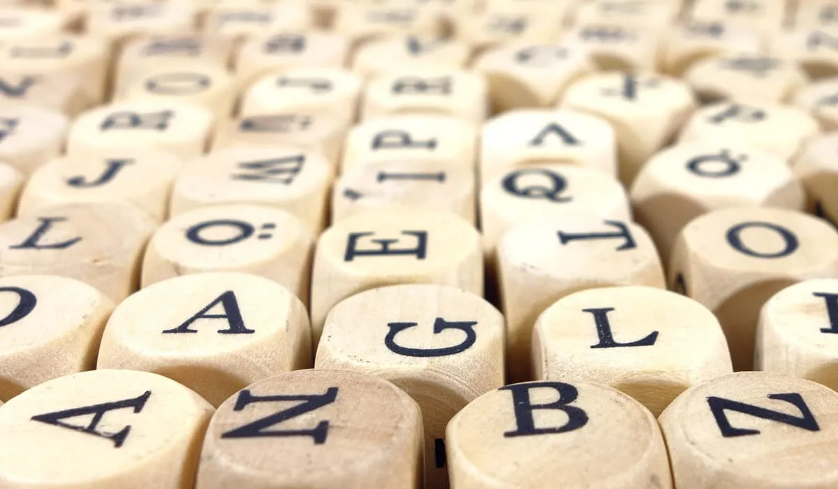 A close-up of wooden letter dice scattered face up, showing a jumble of capital letters.