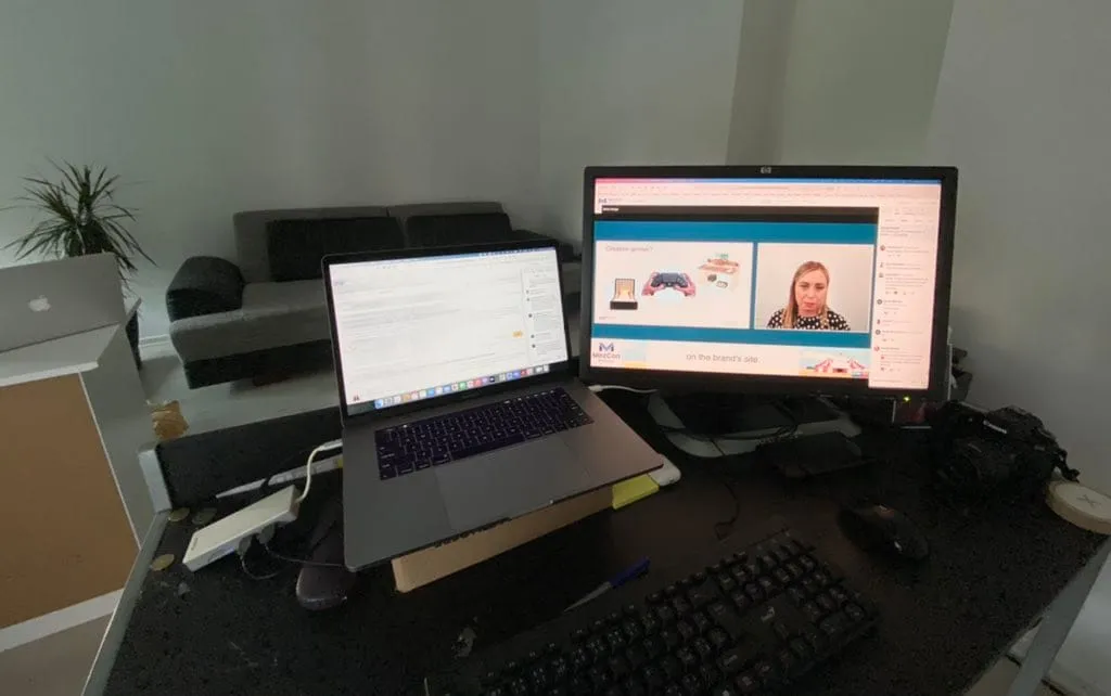 My desk during MozCon Virtual: a laptop open on notes beside a monitor streaming a talk, with the speaker's slide and video on screen.