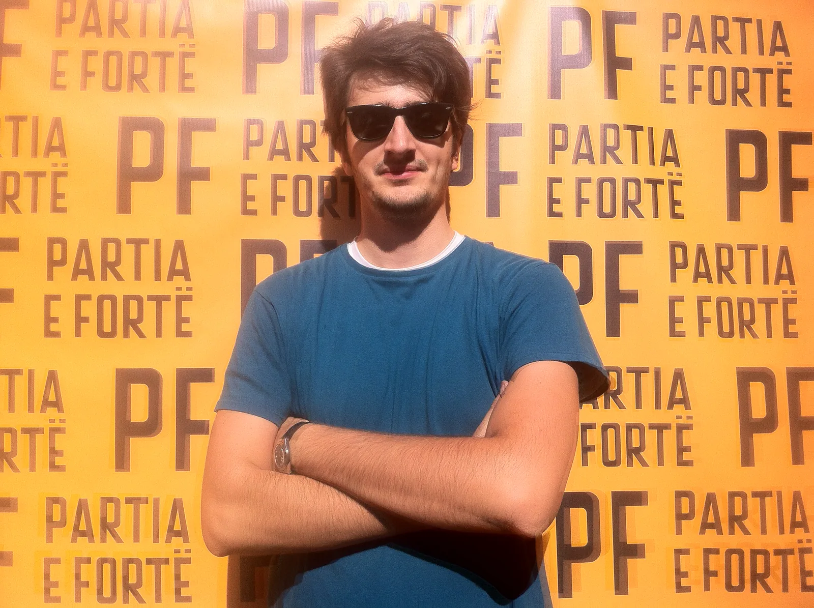 Me in sunglasses, arms crossed, in front of a yellow Partia e Fortë backdrop tiled with the PF logo and the party name.