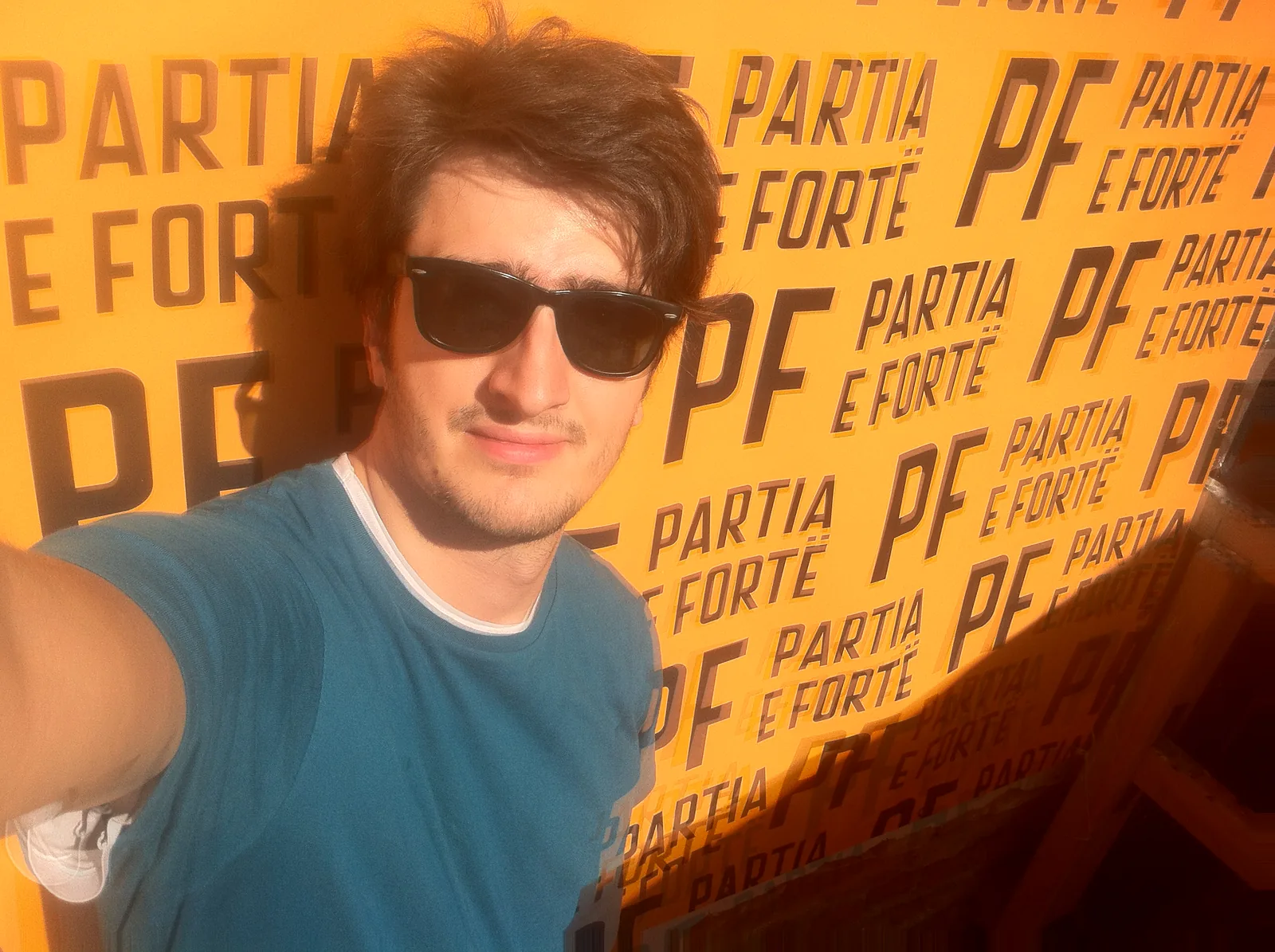 A selfie of me in sunglasses in front of a yellow Partia e Fortë backdrop tiled with the PF logo and the party name.