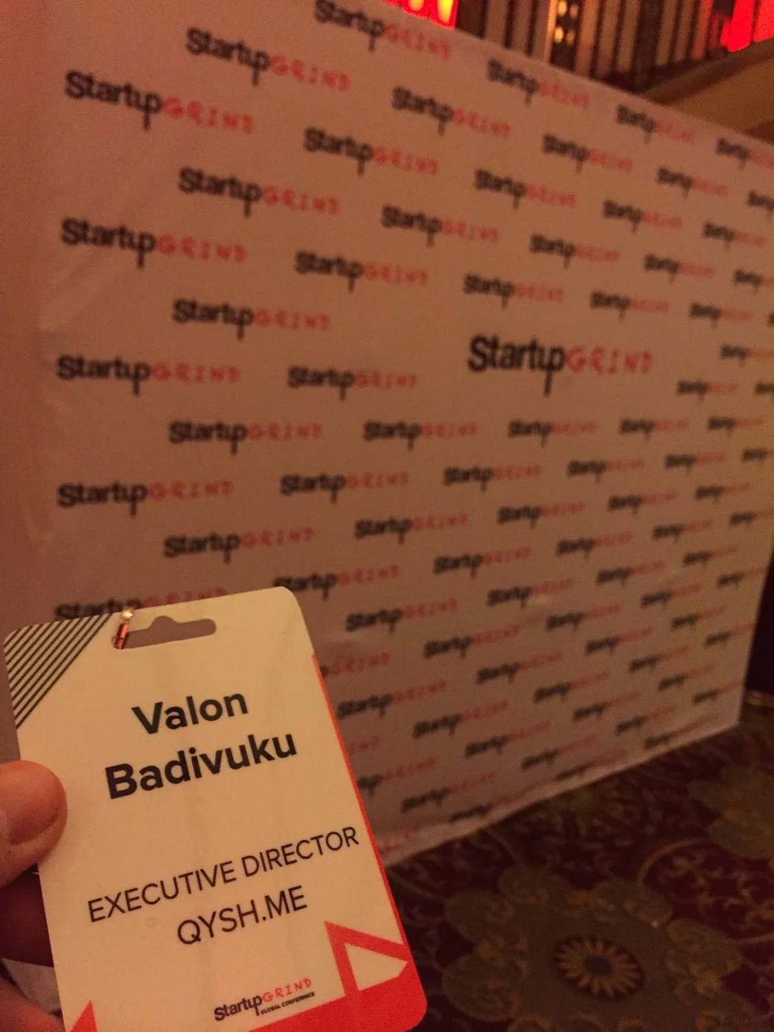 My conference badge in front of a Startup Grind step-and-repeat wall: "Valon Badivuku, Executive Director, QYSH.ME."