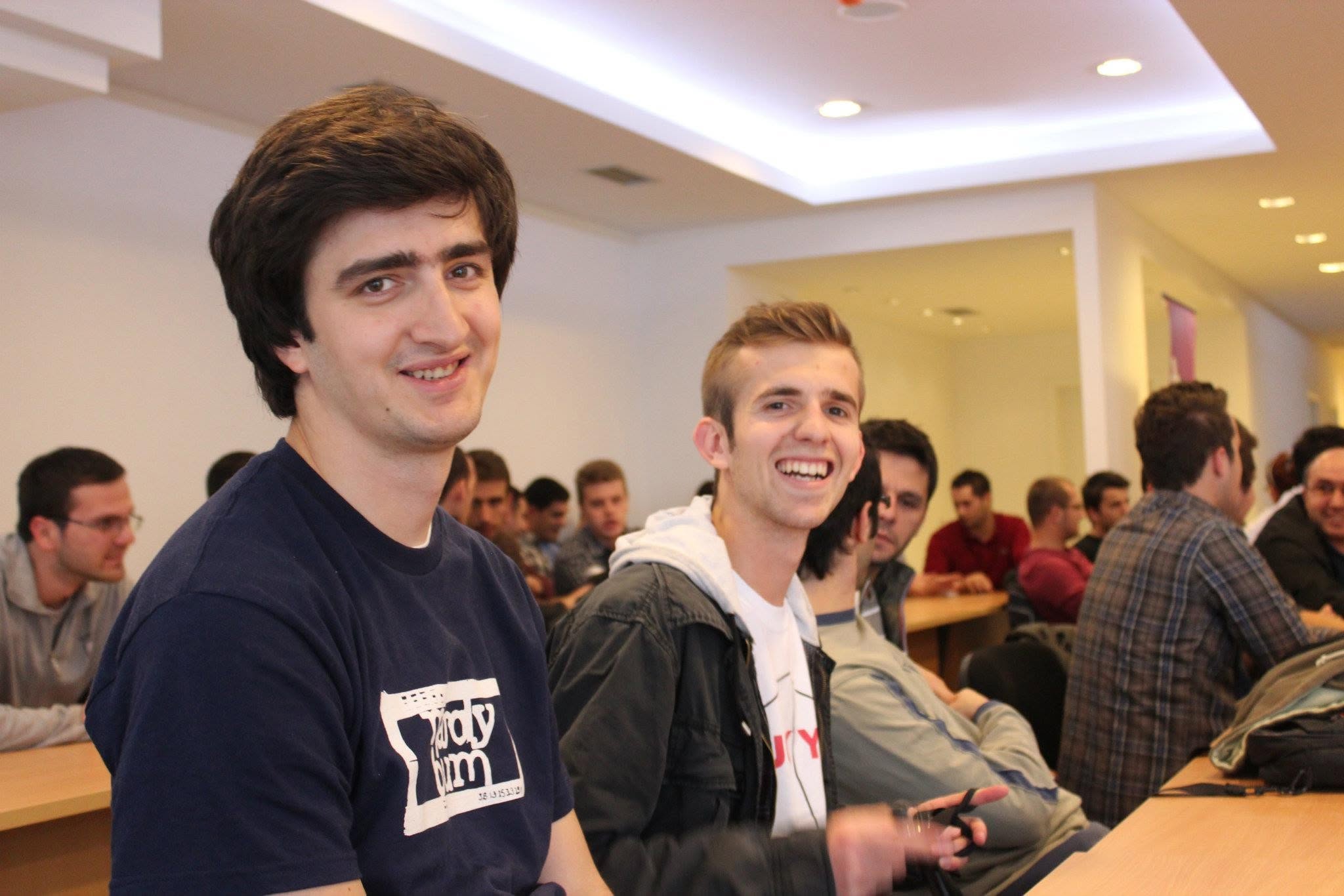 Me on the left and Fisnik Sylka on the right, sitting at a long table in a room full of participants at Startup Weekend Prishtina.