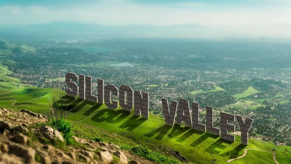 The words SILICON VALLEY built as giant hillside letters, in the style of the Hollywood sign, above a green valley of suburbs and trees.